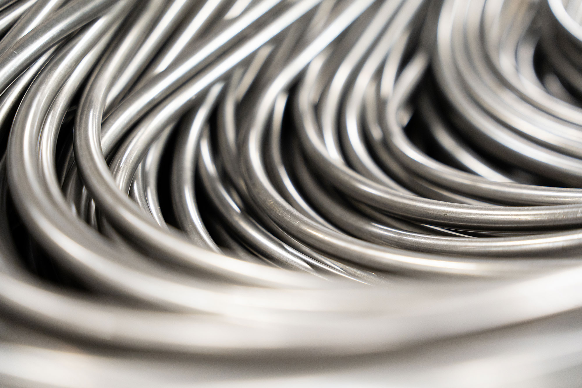 Close-up of smooth, silver wires intricately intertwined, creating flowing wave patterns. The metallic textures convey a sleek, modern feel.