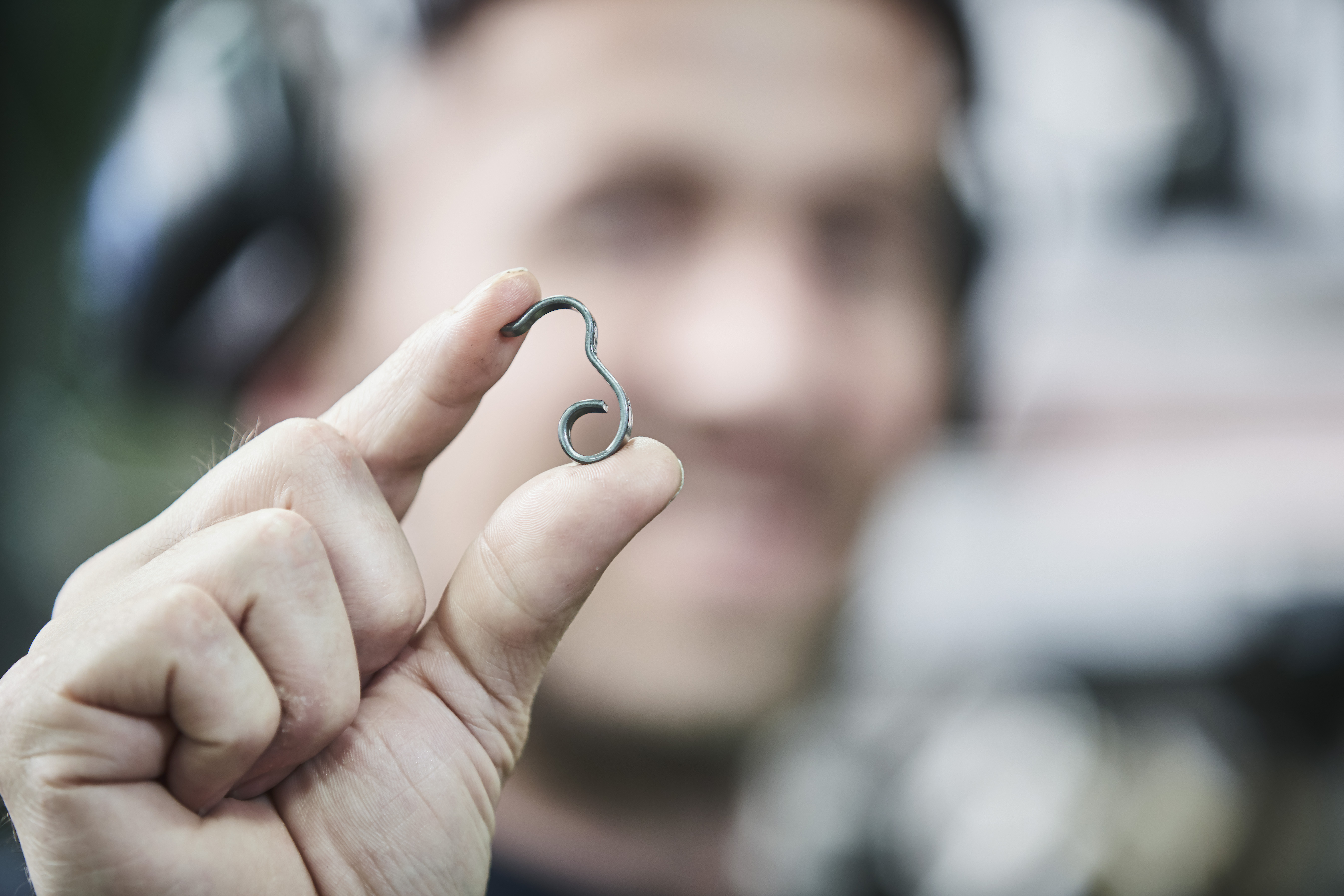 A person holds a tiny wire form spring between their fingers, with a blurred background. 