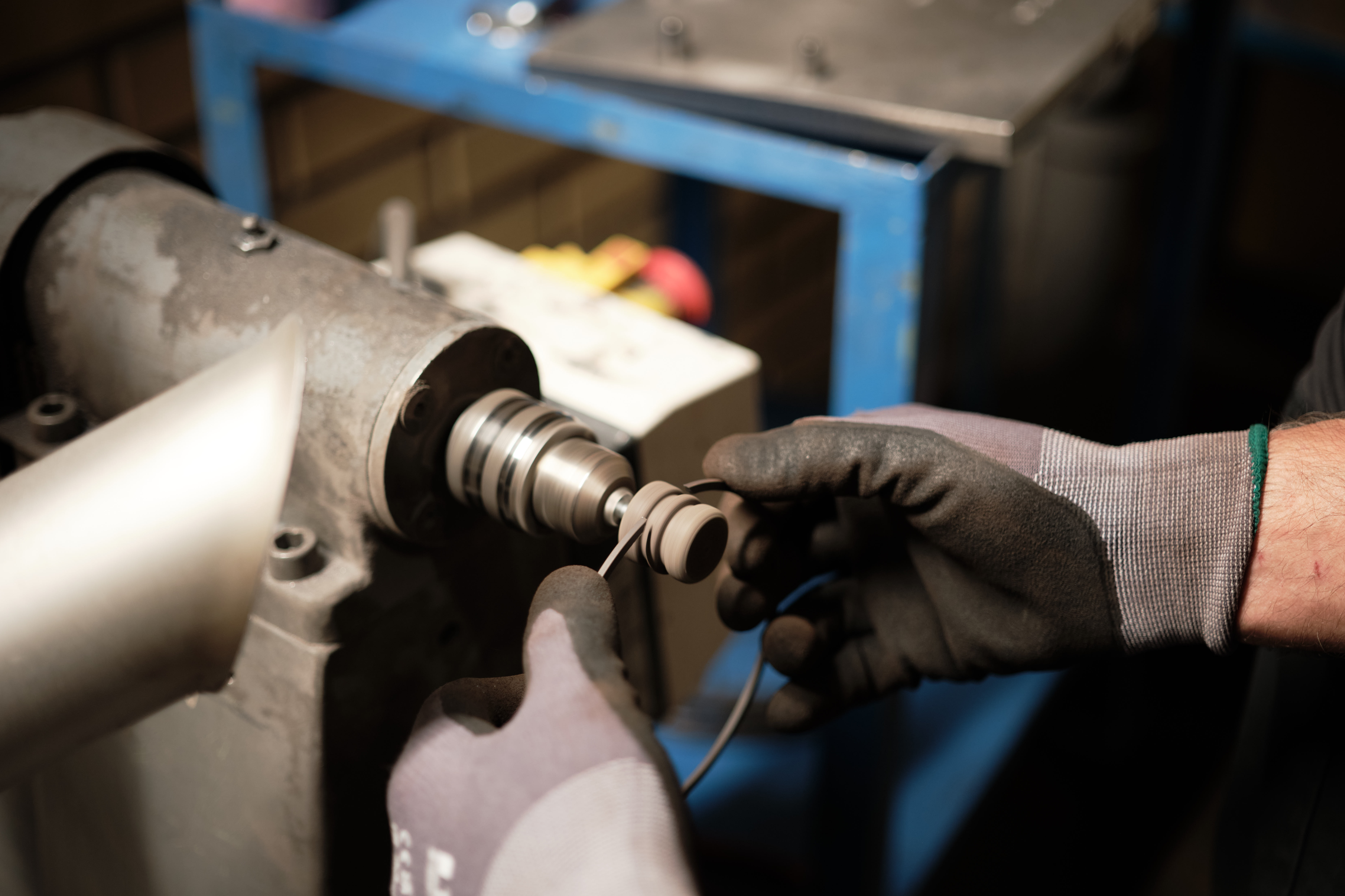 A person wearing black gloves carefully inserts a metal part into a lathe machine, highlighting precision and focus in a workshop setting.