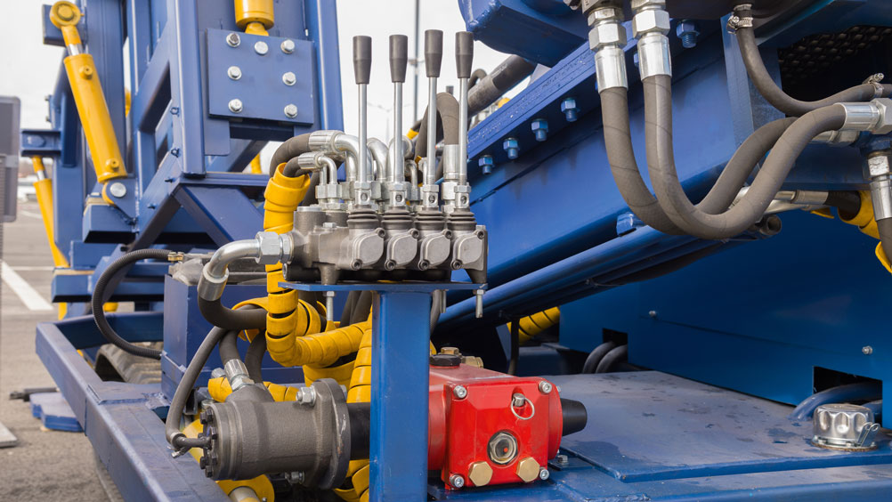 Close-up of industrial machinery featuring blue and yellow components with hydraulic levers and pipes. 