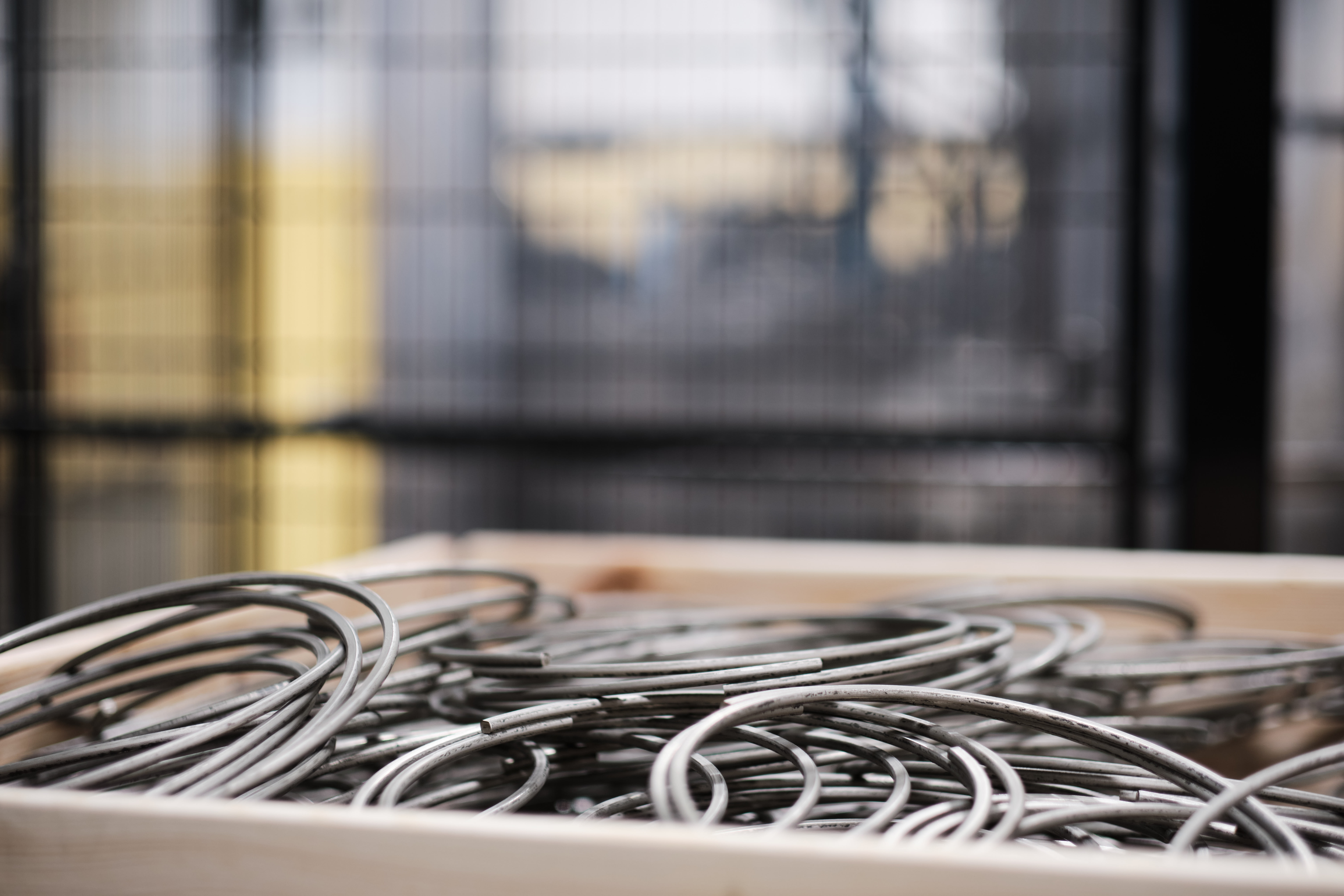 A wooden box filled with tangled wire rings sits in a well-lit, modern room. The background features large windows, creating a calm, industrial atmosphere.
