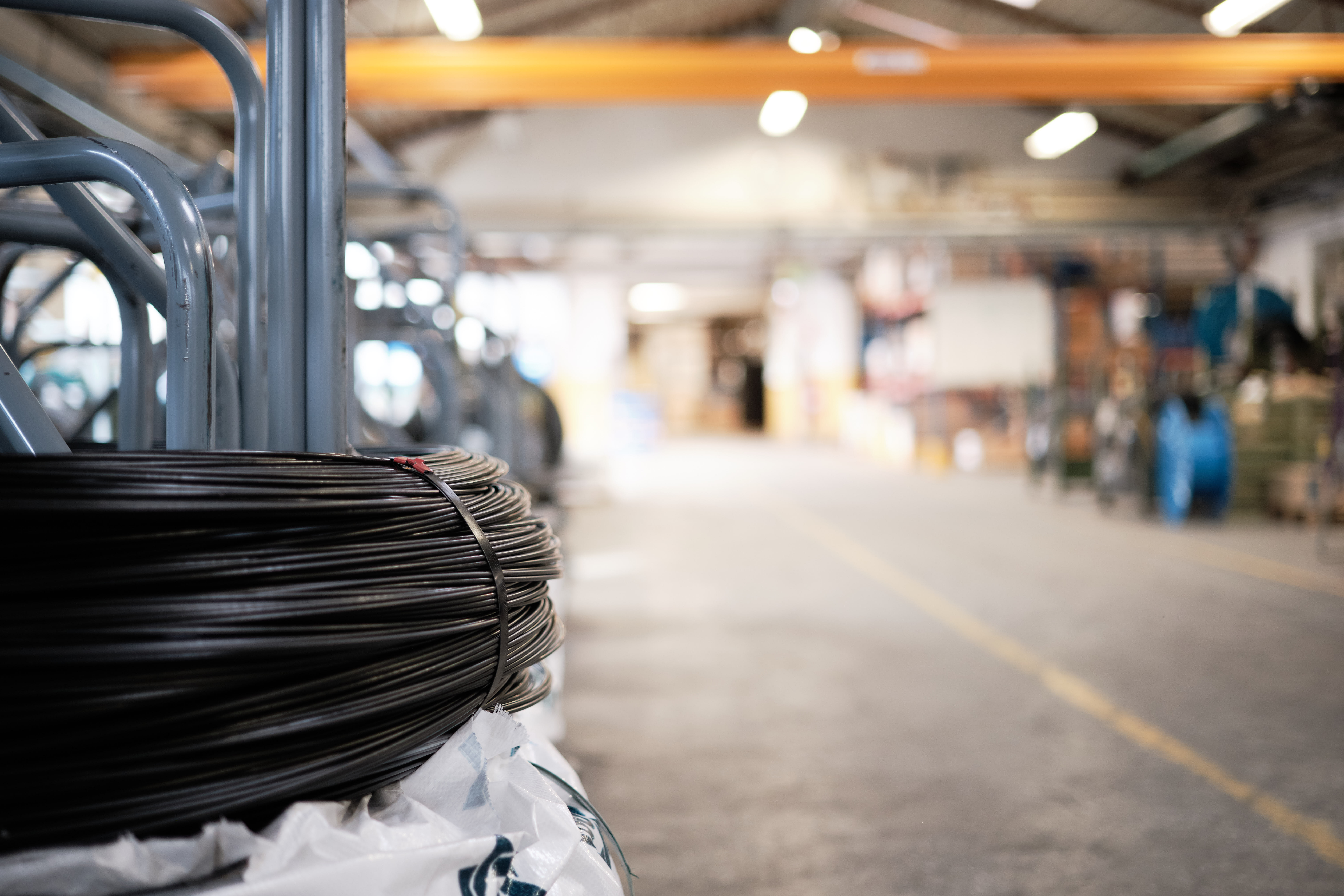 A stack of coiled black hoses in focus in a spacious industrial warehouse. The background is blurred, with shelves and equipment visible.