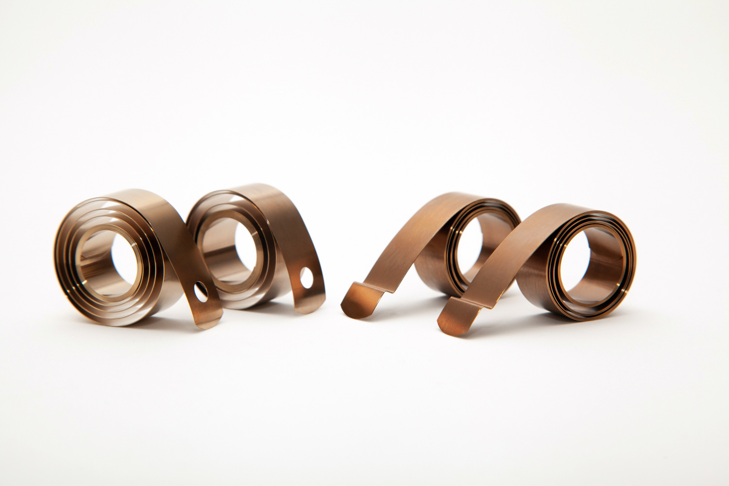 Close-up of four flat springs, curled in spiral shapes on a white background. The smooth texture and warm brown tones create an artistic, natural feel.