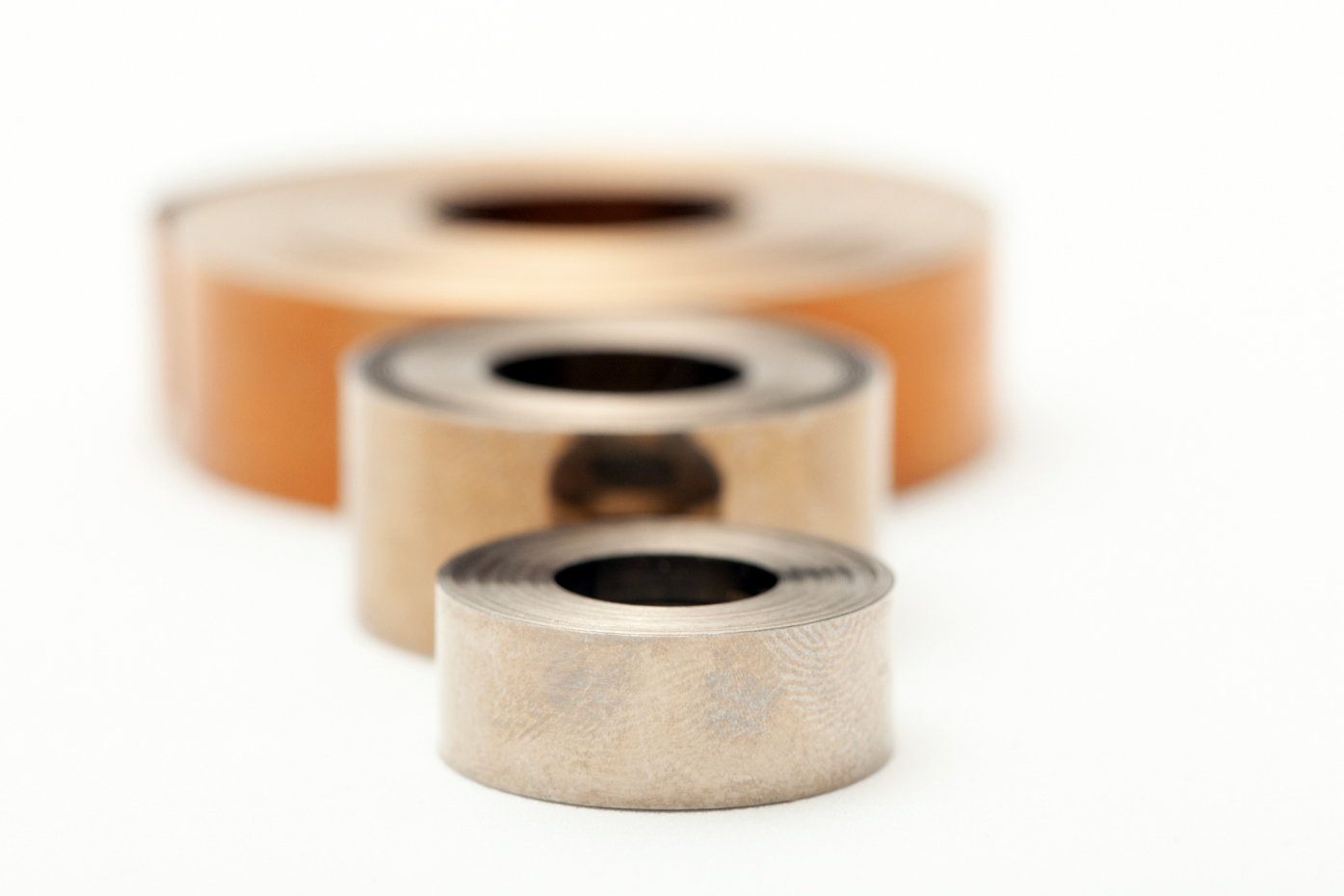 Three stacked flat springs, varying in size against a white background. The tone is industrial and minimalistic.