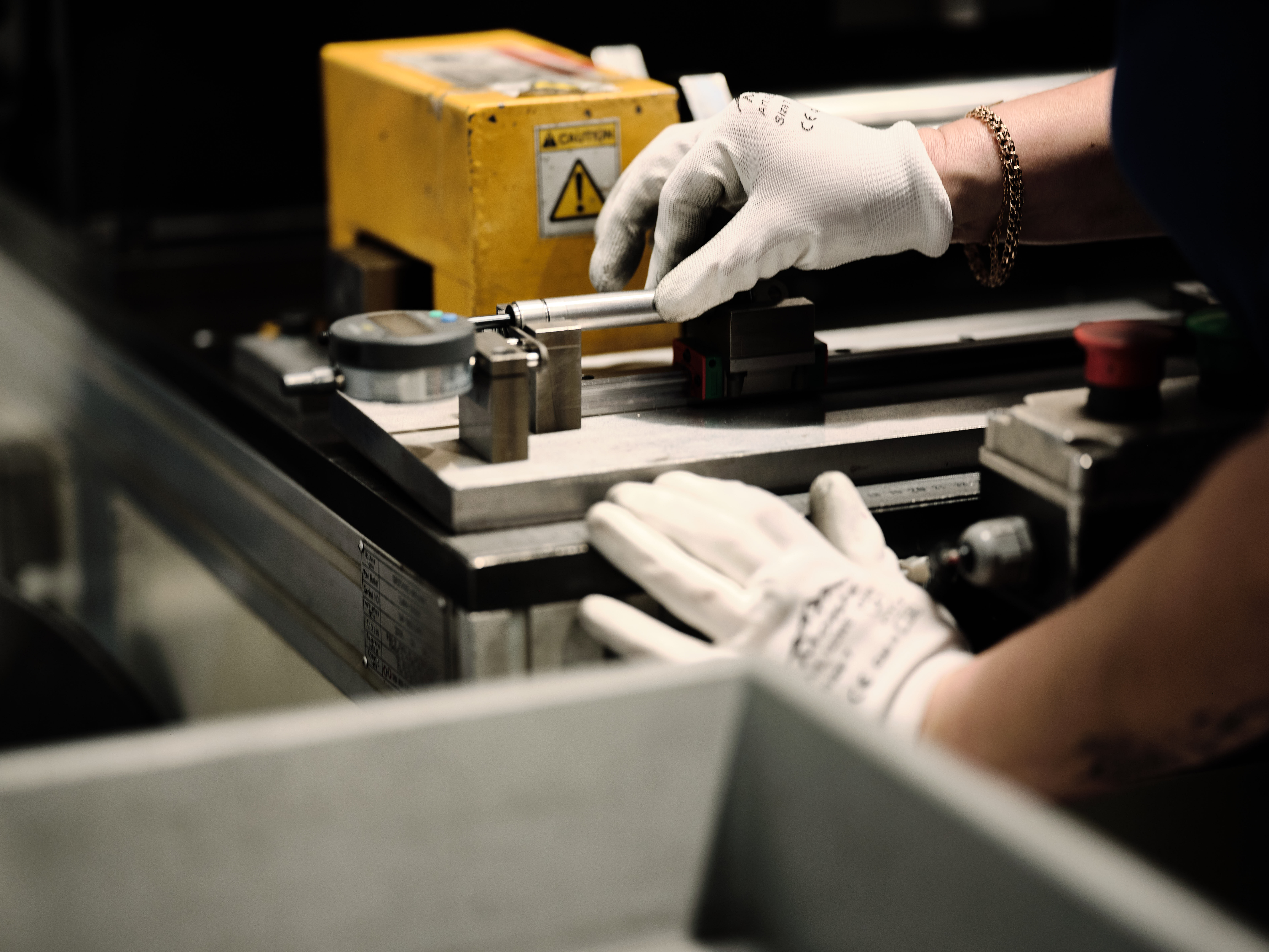 Person wearing white gloves works with a dynamic gas spring on a metal table. A part of the machine is yellow.