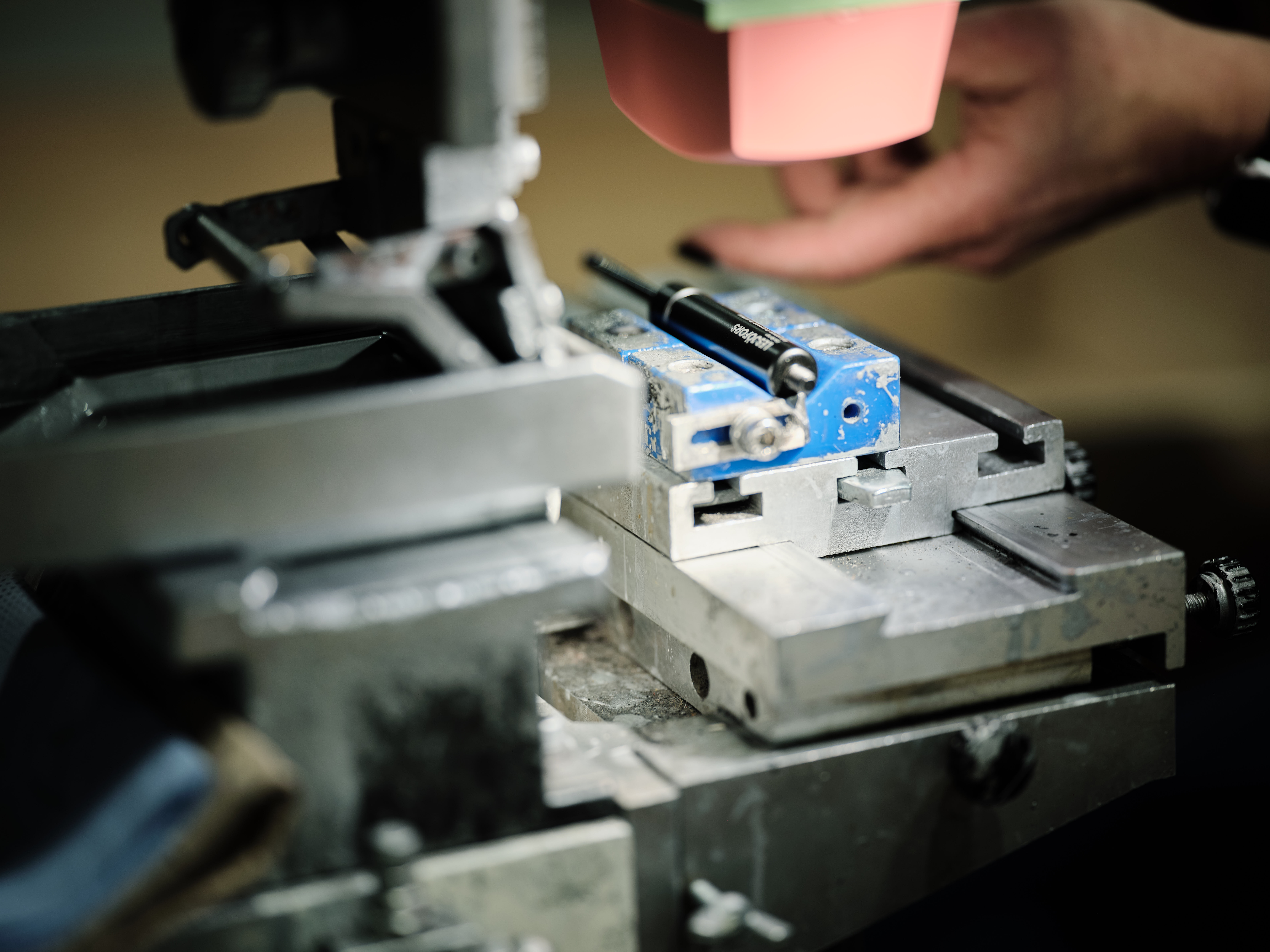 A person's hands adjust a metal gas spring on a precision machining tool. The gas spring is metallic coloured.
