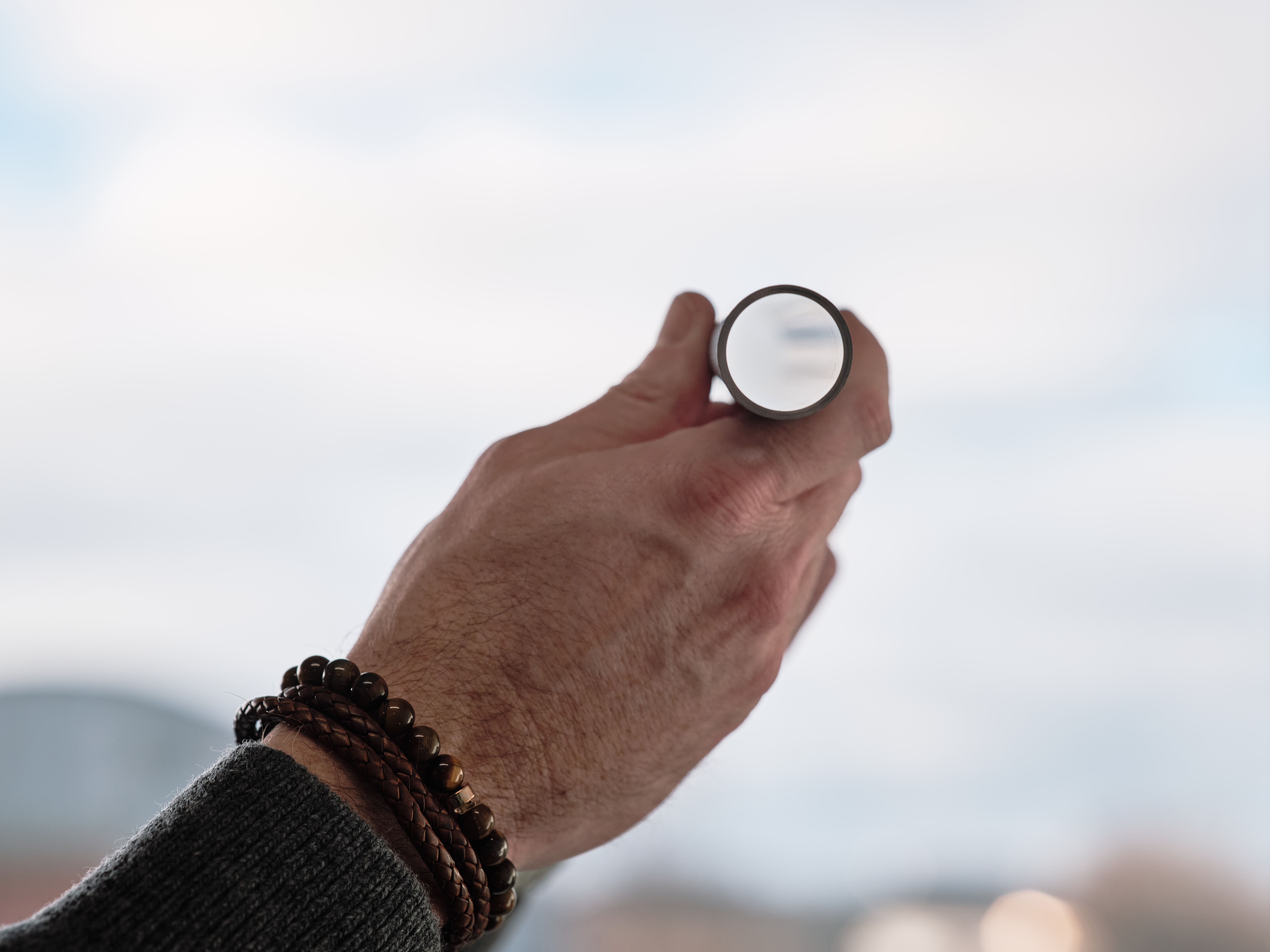 A hand wearing bracelets holds a gas spring, up to the sky, reflecting clouds.