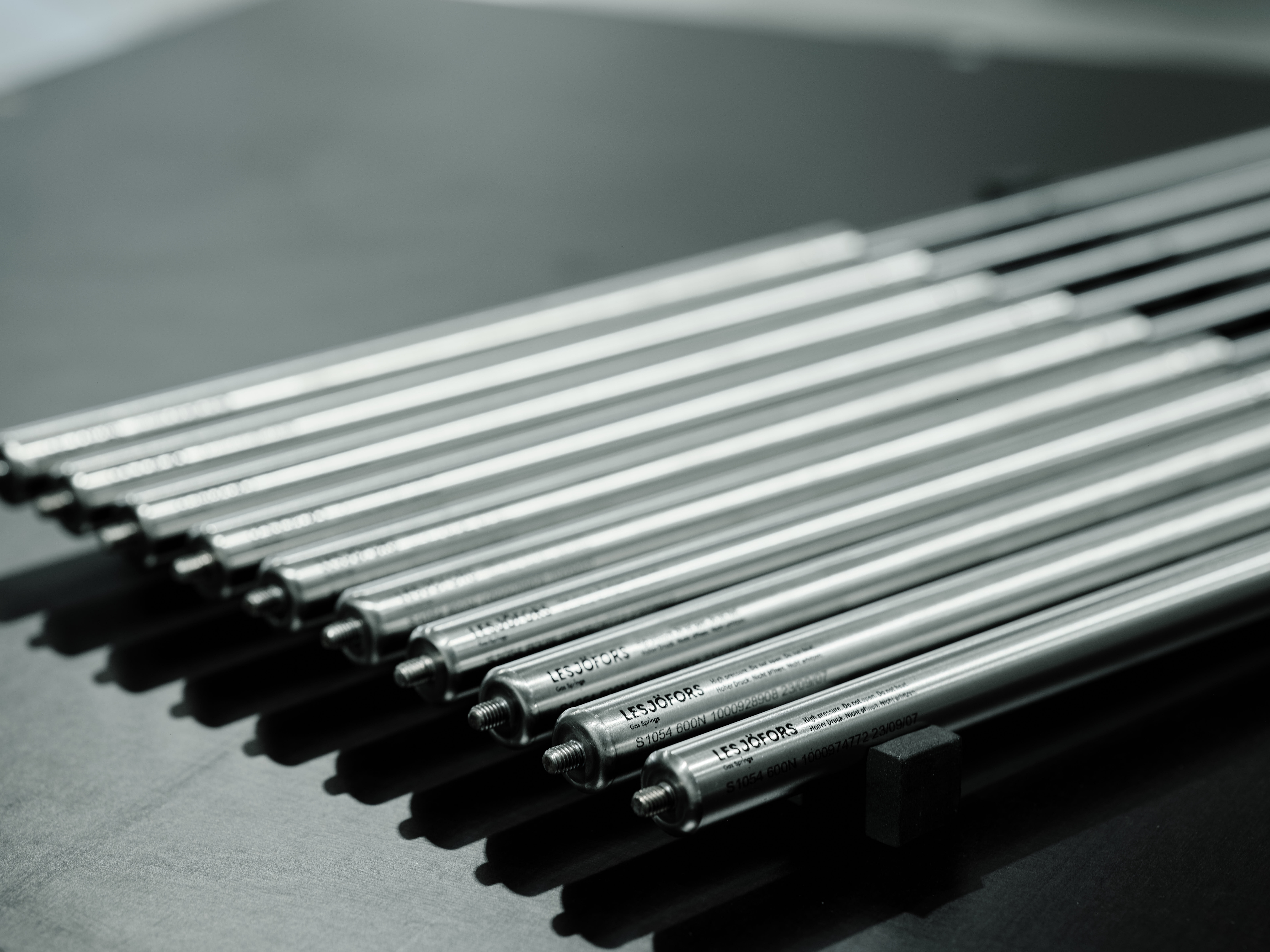 Close-up of shiny metal gas springs aligned in parallel on a dark surface, creating a sleek, industrial appearance.