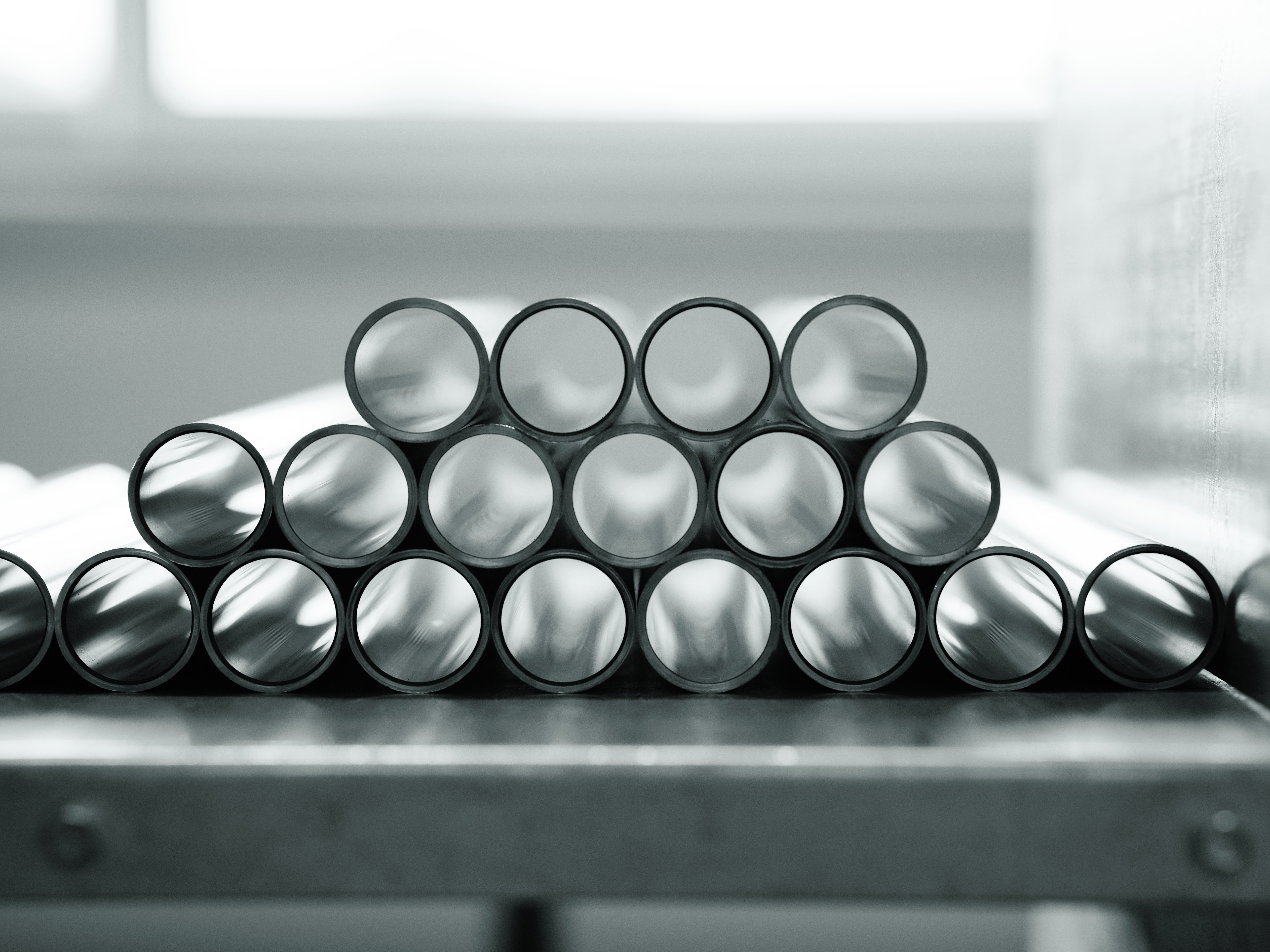 Stacked metal tubes in pyramid form on a table, set in a monochrome laboratory. Bright lighting creates a clinical, organized atmosphere.