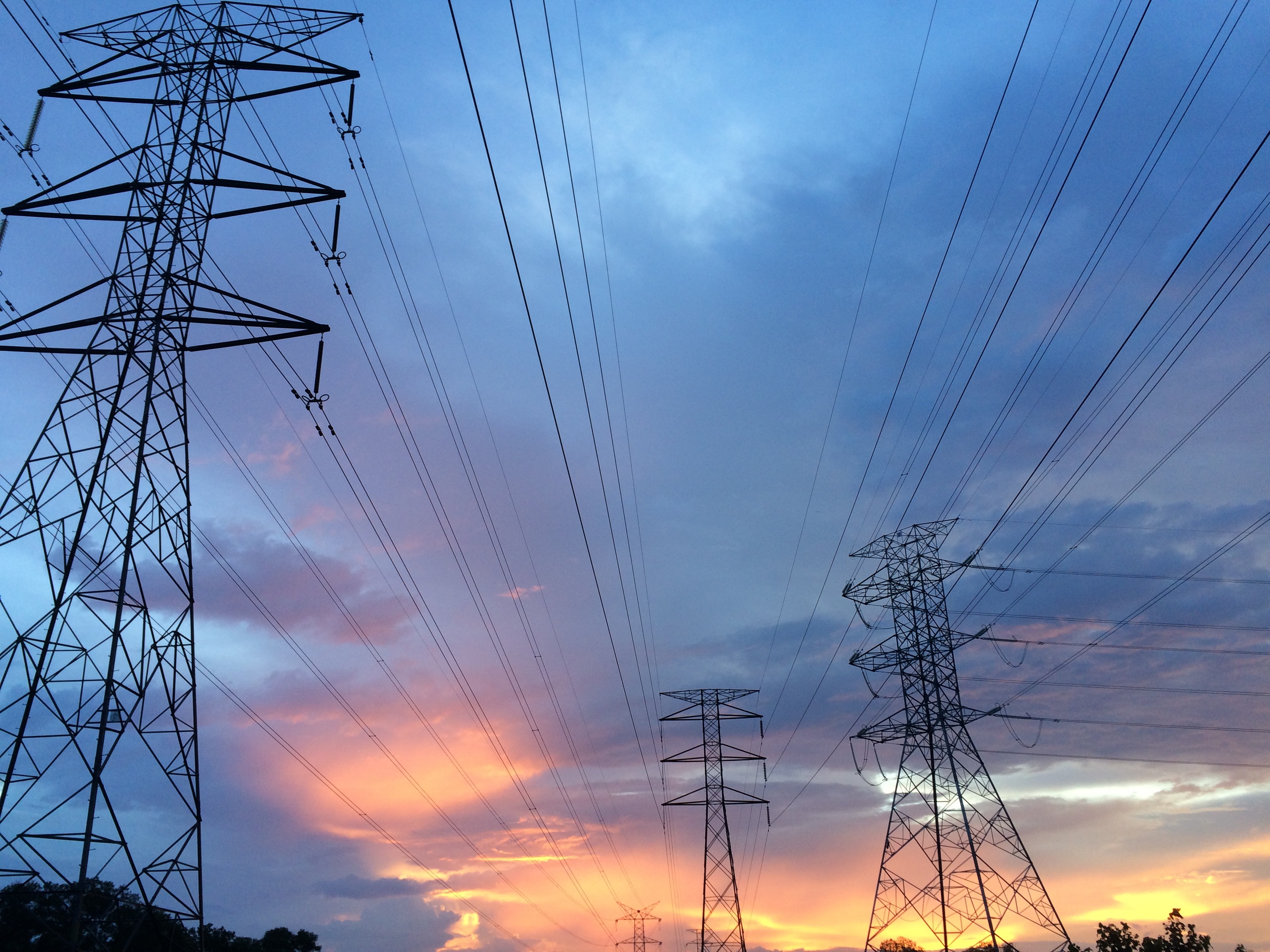 Electricity pylons and power lines silhouetted against a colorful sunset sky.
