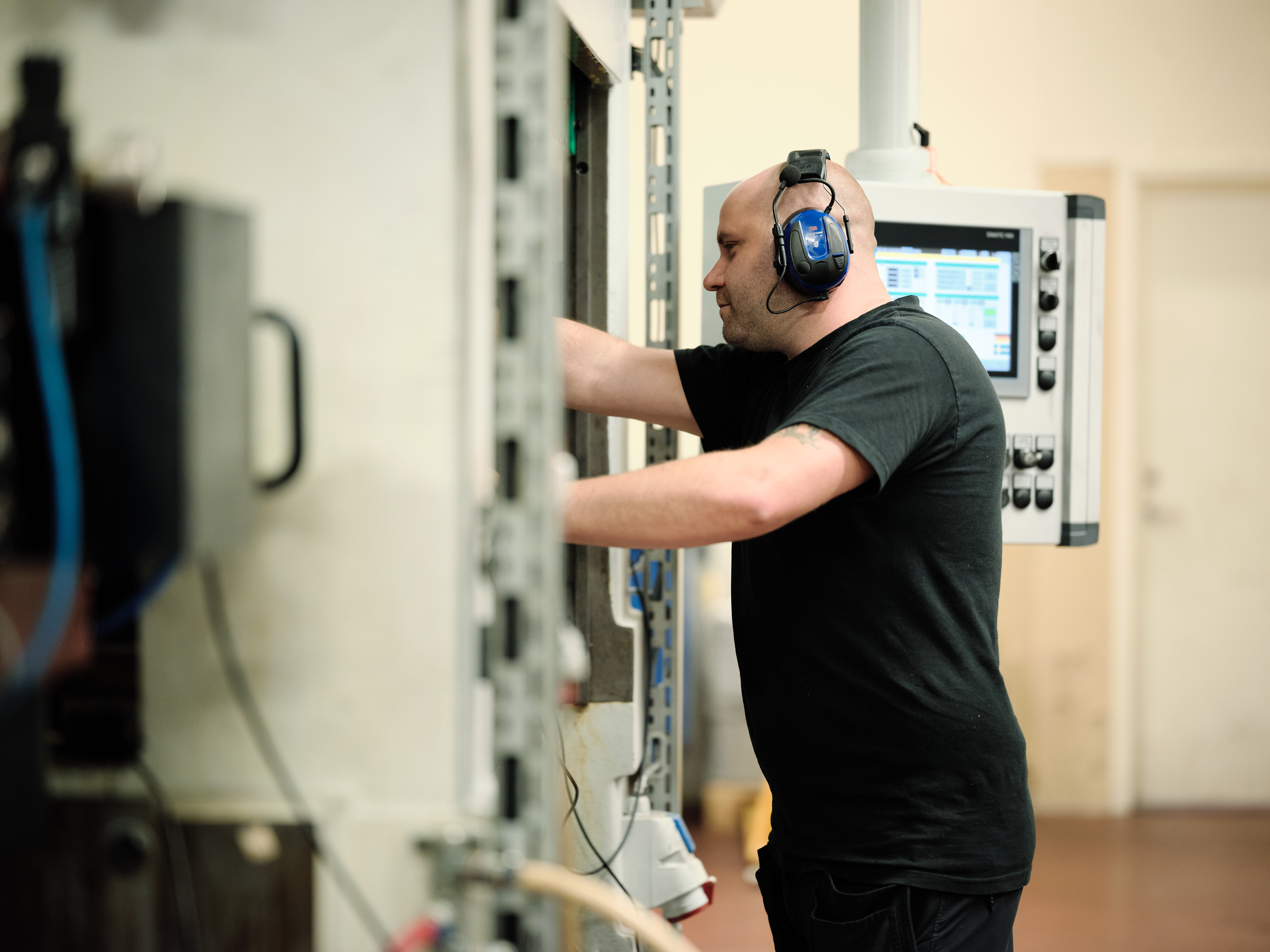 A factory worker wearing hearing protection operating industrial machinery.