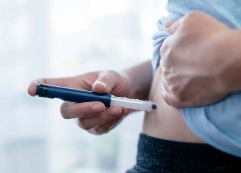 A person using a pen injector to administer an insulin injection into their abdomen.