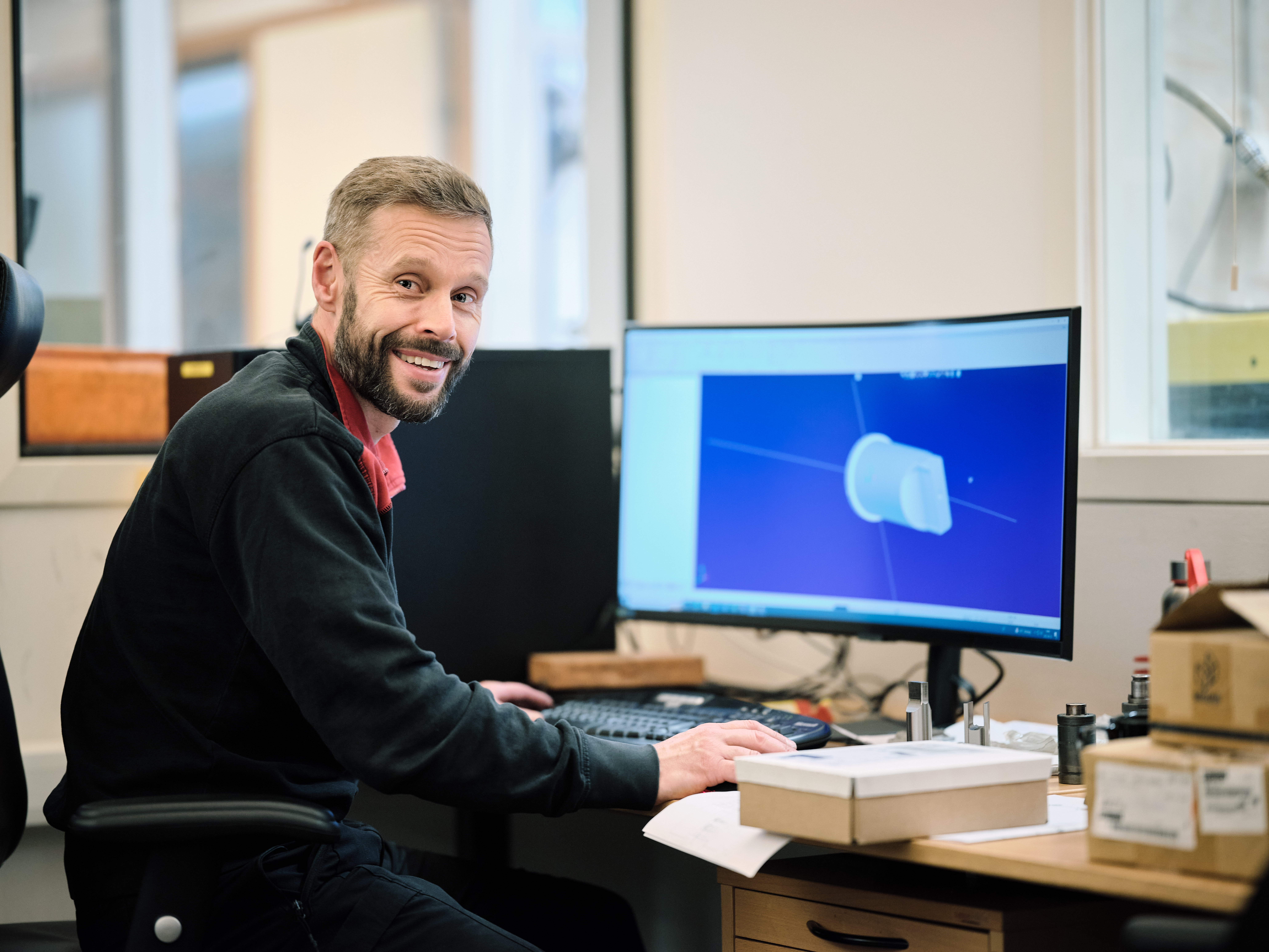 An engineer working at a computer, designing a 3D model of a metal component.