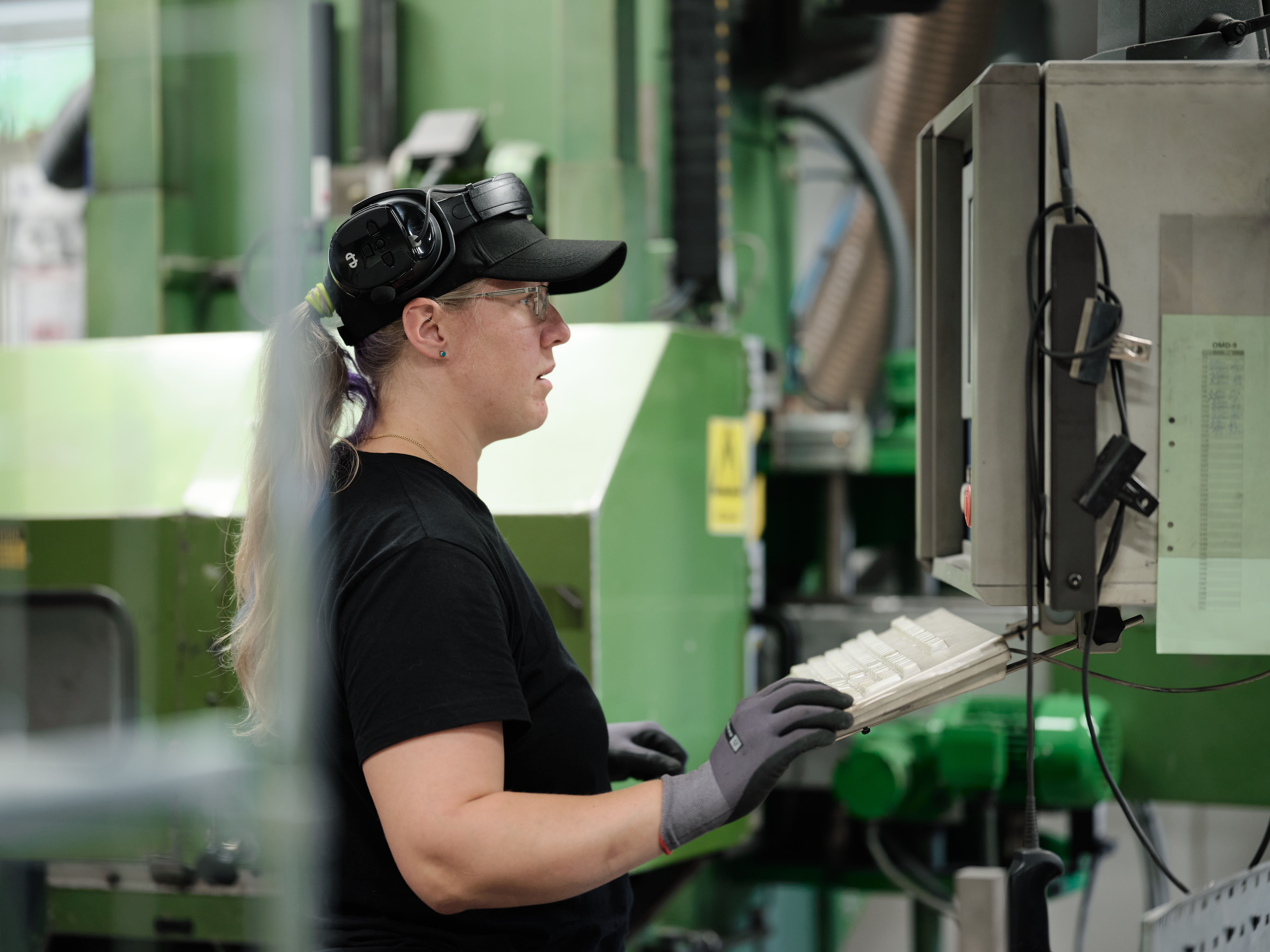 A factory worker wearing safety glasses and hearing protection operating a machine using a control panel.