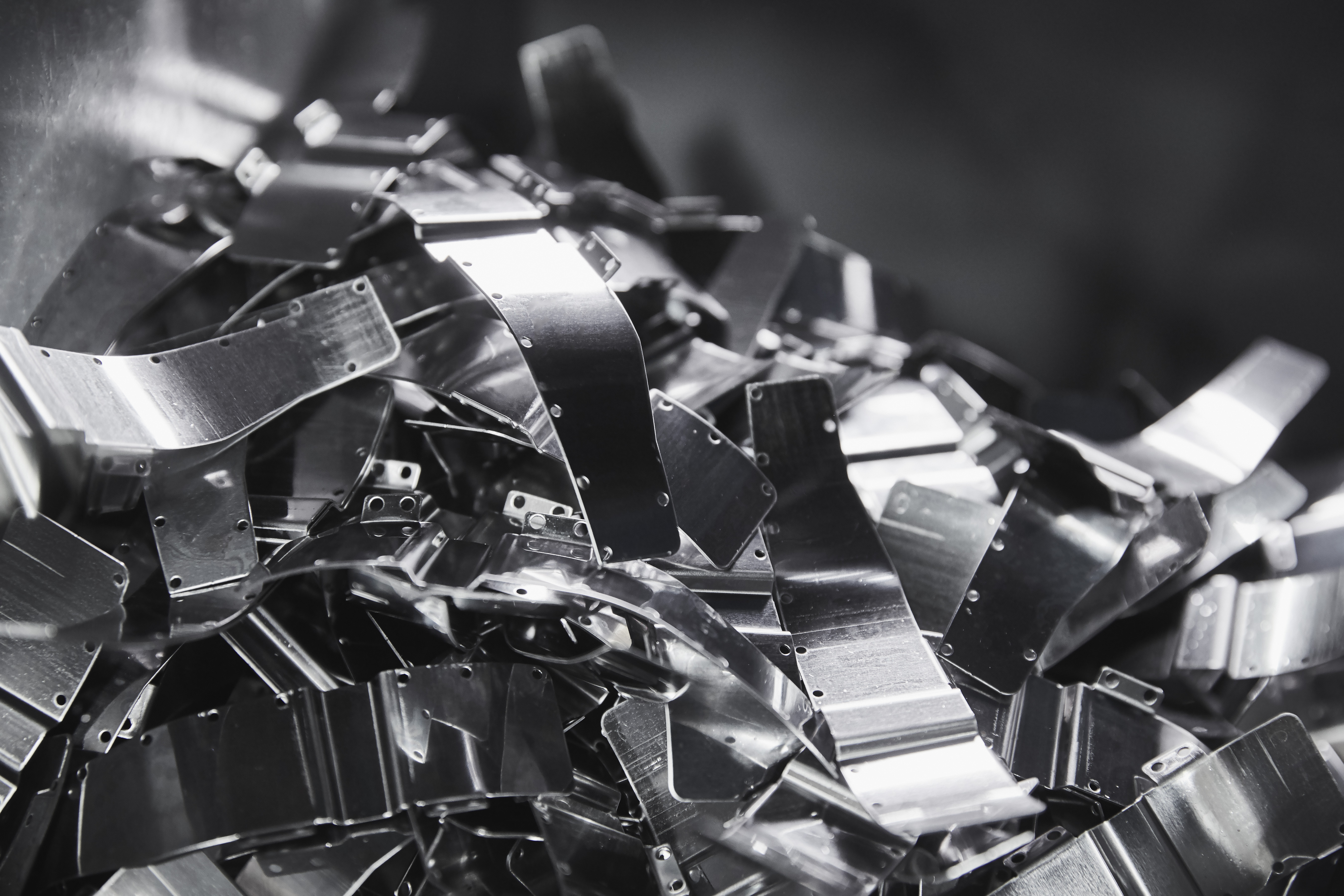 A pile of shiny stamped metal parts with curved forms and small holes.