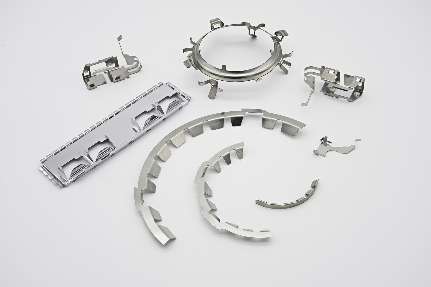 Assortment of silver progressive die stamped parts showing intricate cut-outs, tabs, and formed edges.