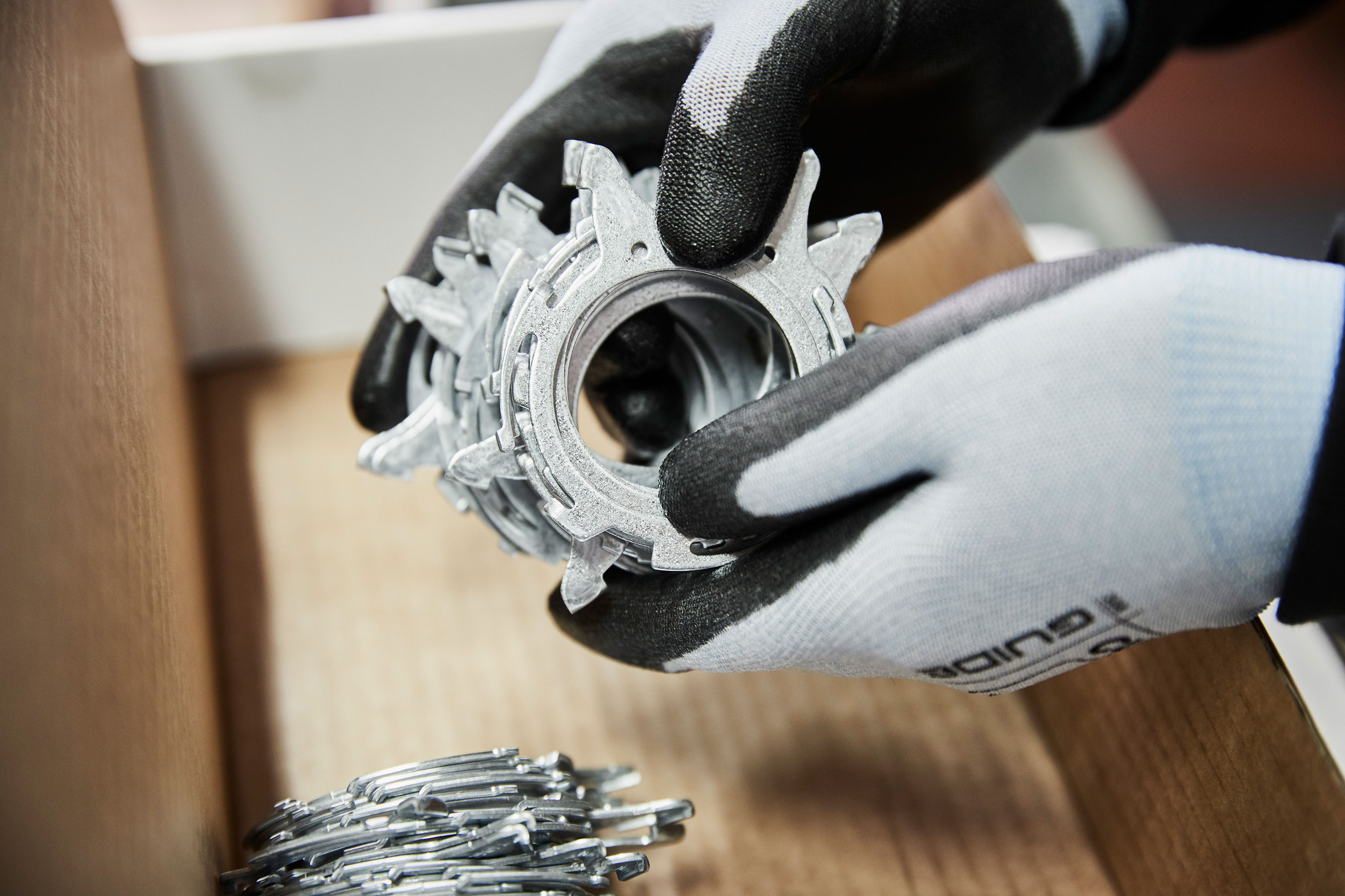 A factory worker’s gloved hands holding a stack of stamped metal parts.