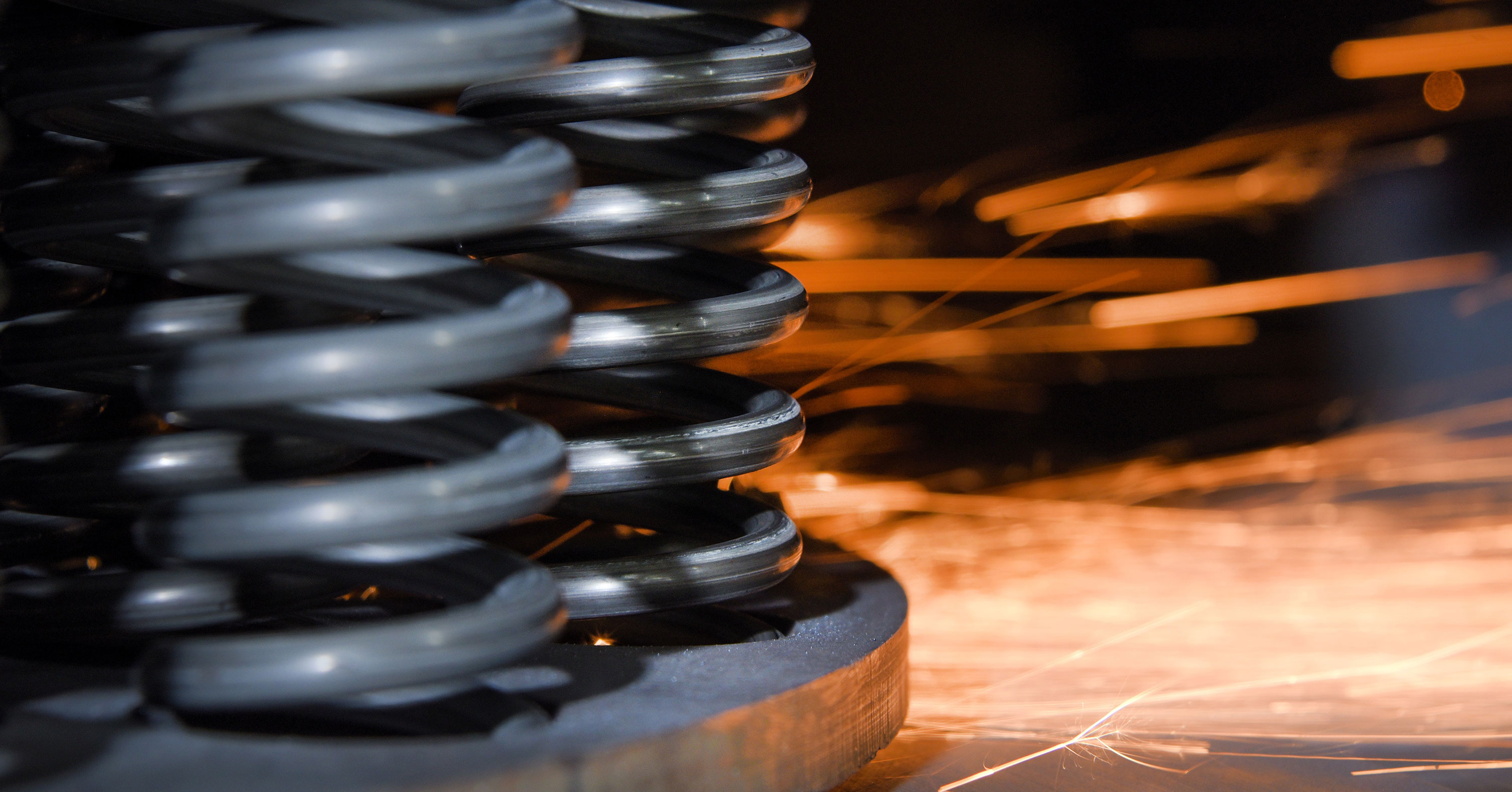 Close-up of dark gray metal compression springs with sparks flying during a machining process.