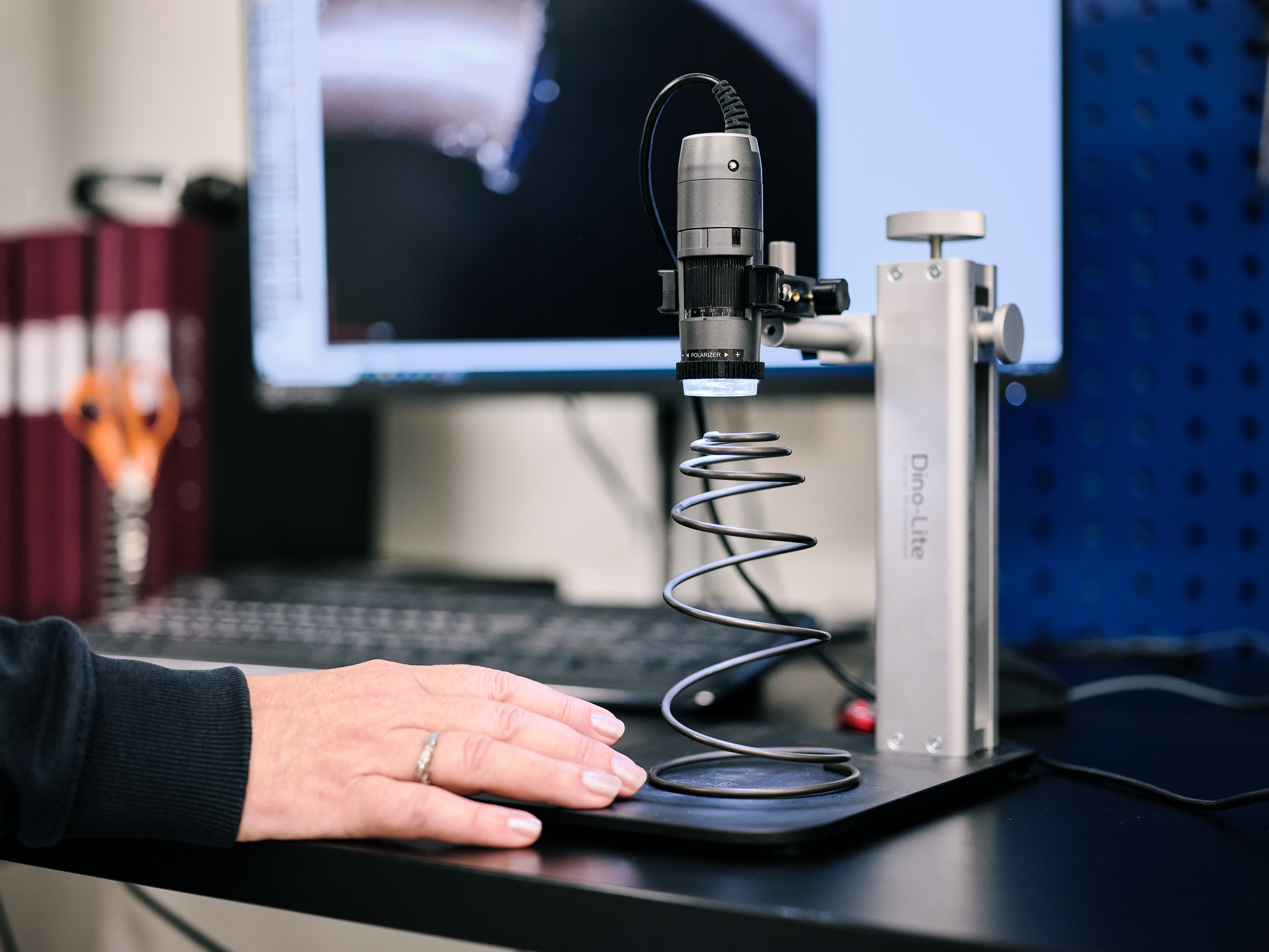 Technician inspecting a conical compression spring under a microscope at a workstation.