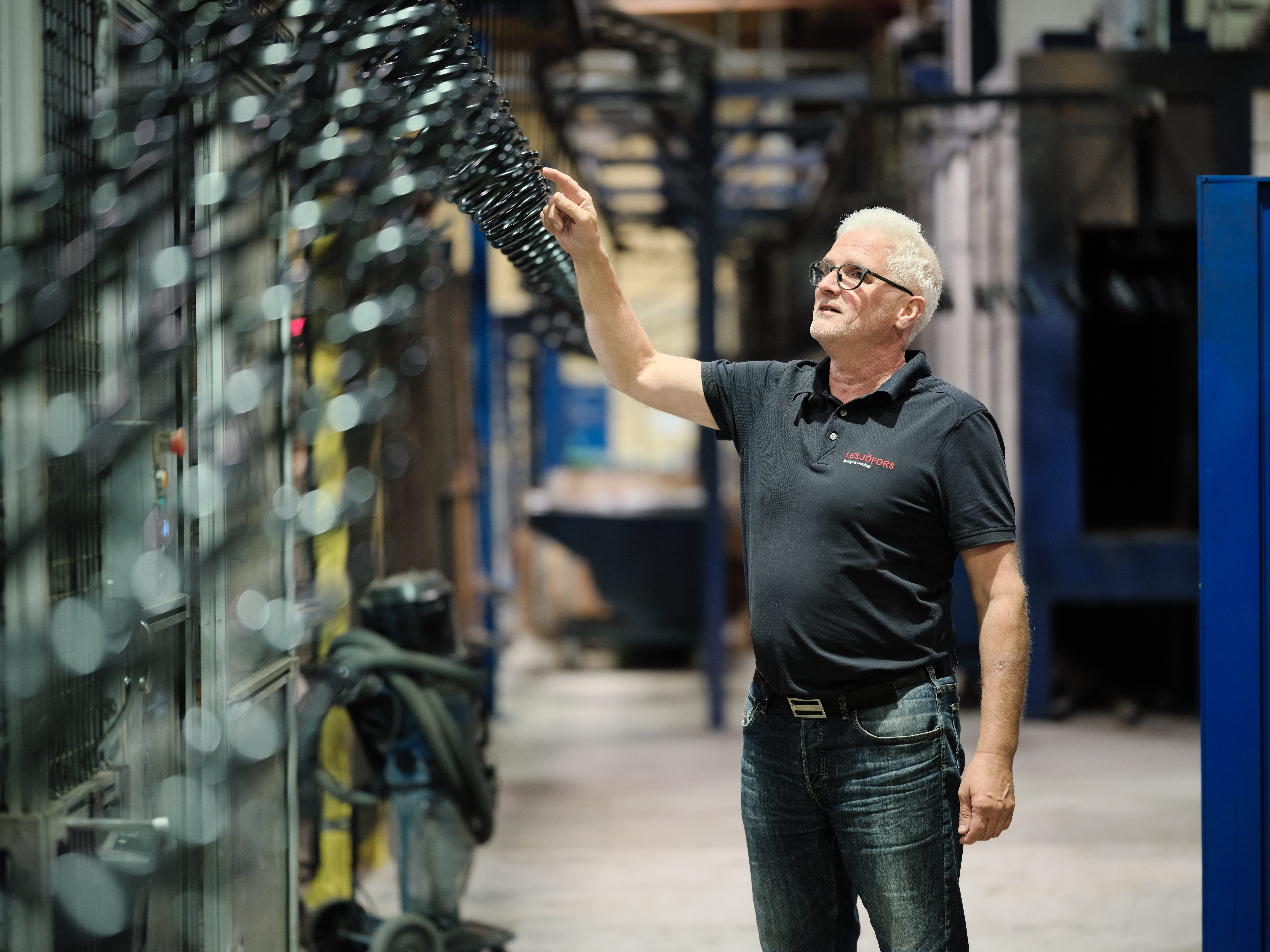 Lesjöfors worker examining a row of black metal springs in a manufacturing facility.