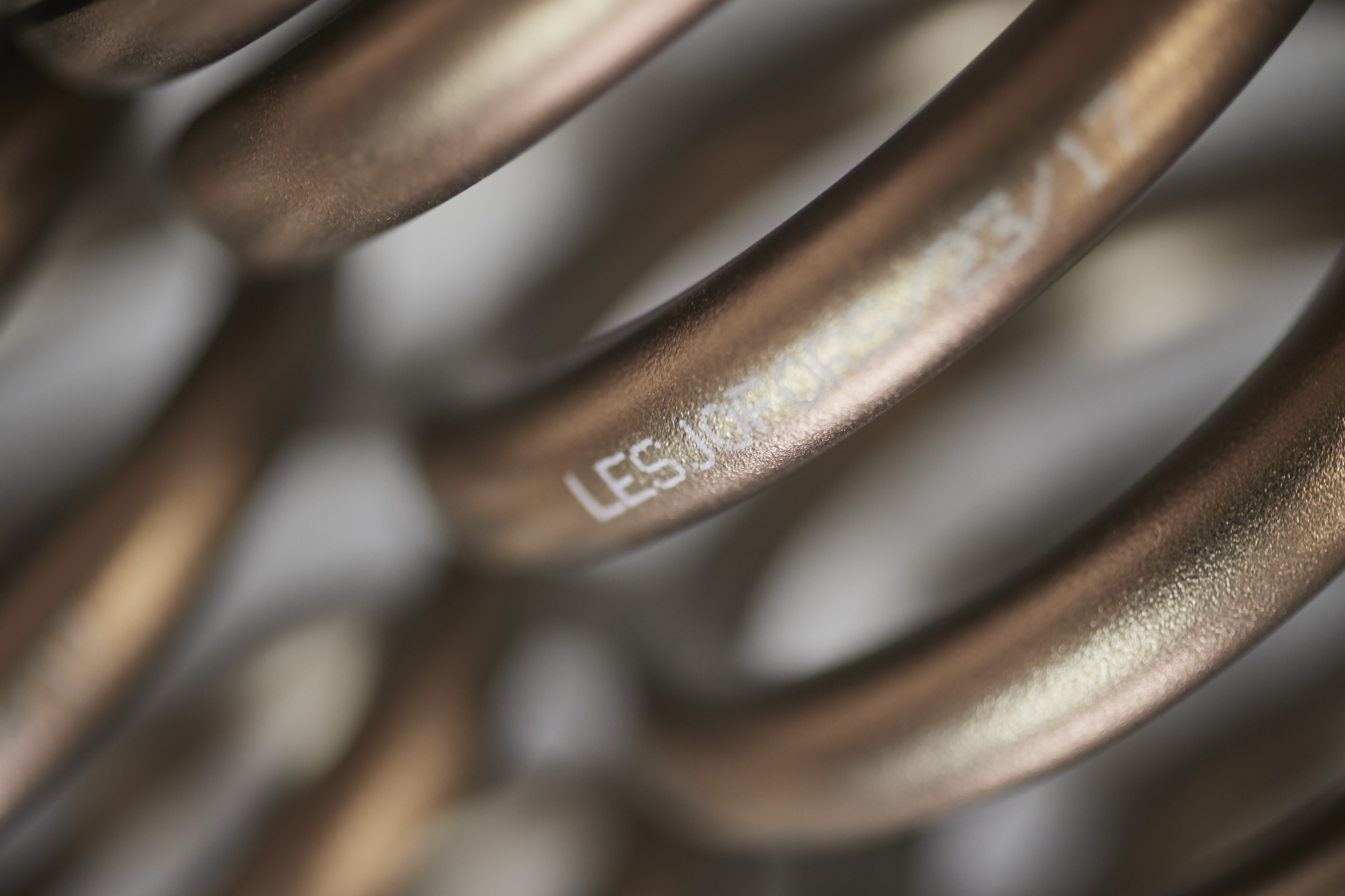 Close-up of a bronze-colored metal coil spring with the Lesjöfors brand name printed on its surface.