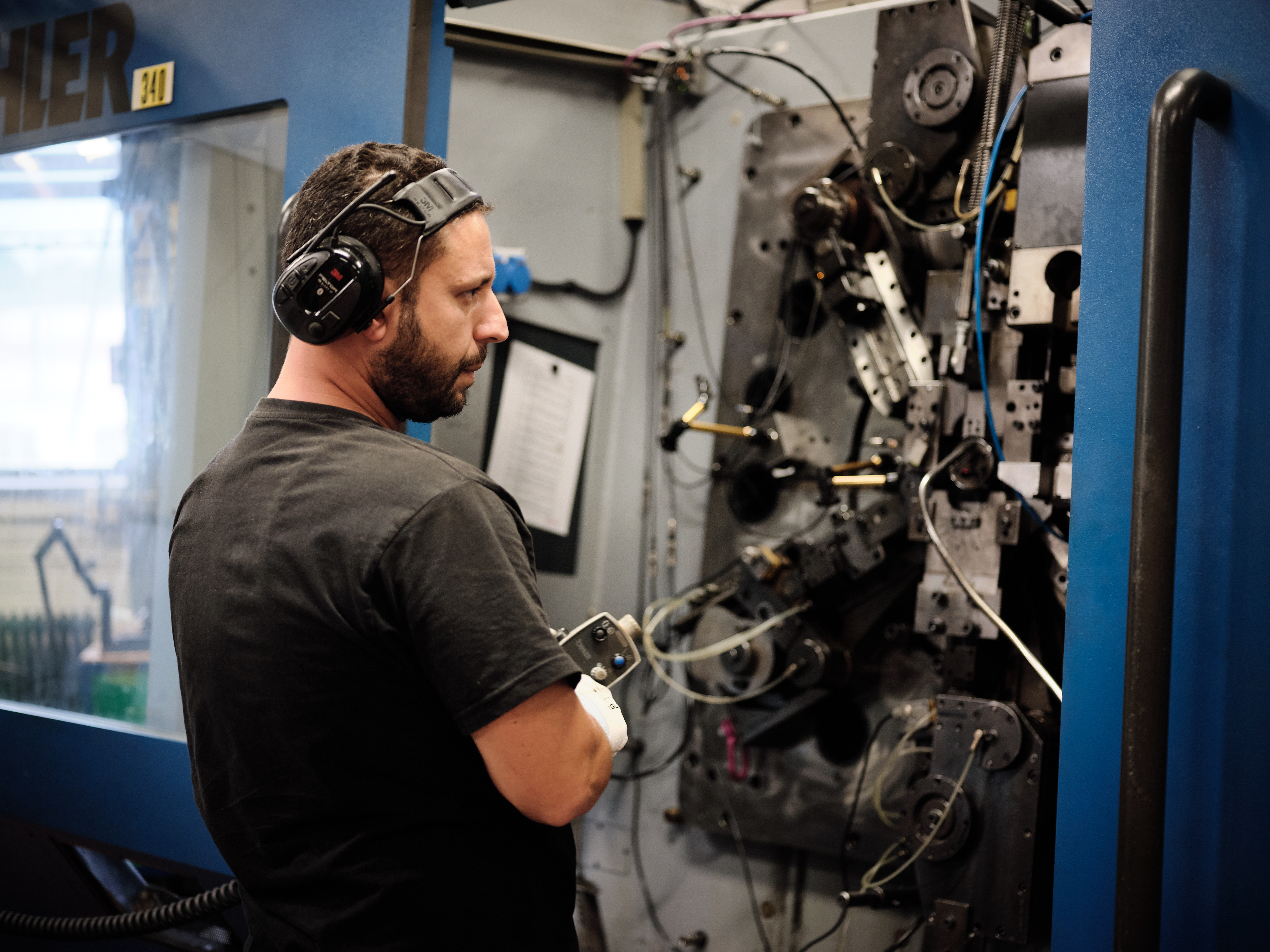 Worker wearing hearing protection operating an industrial spring manufacturing machine.