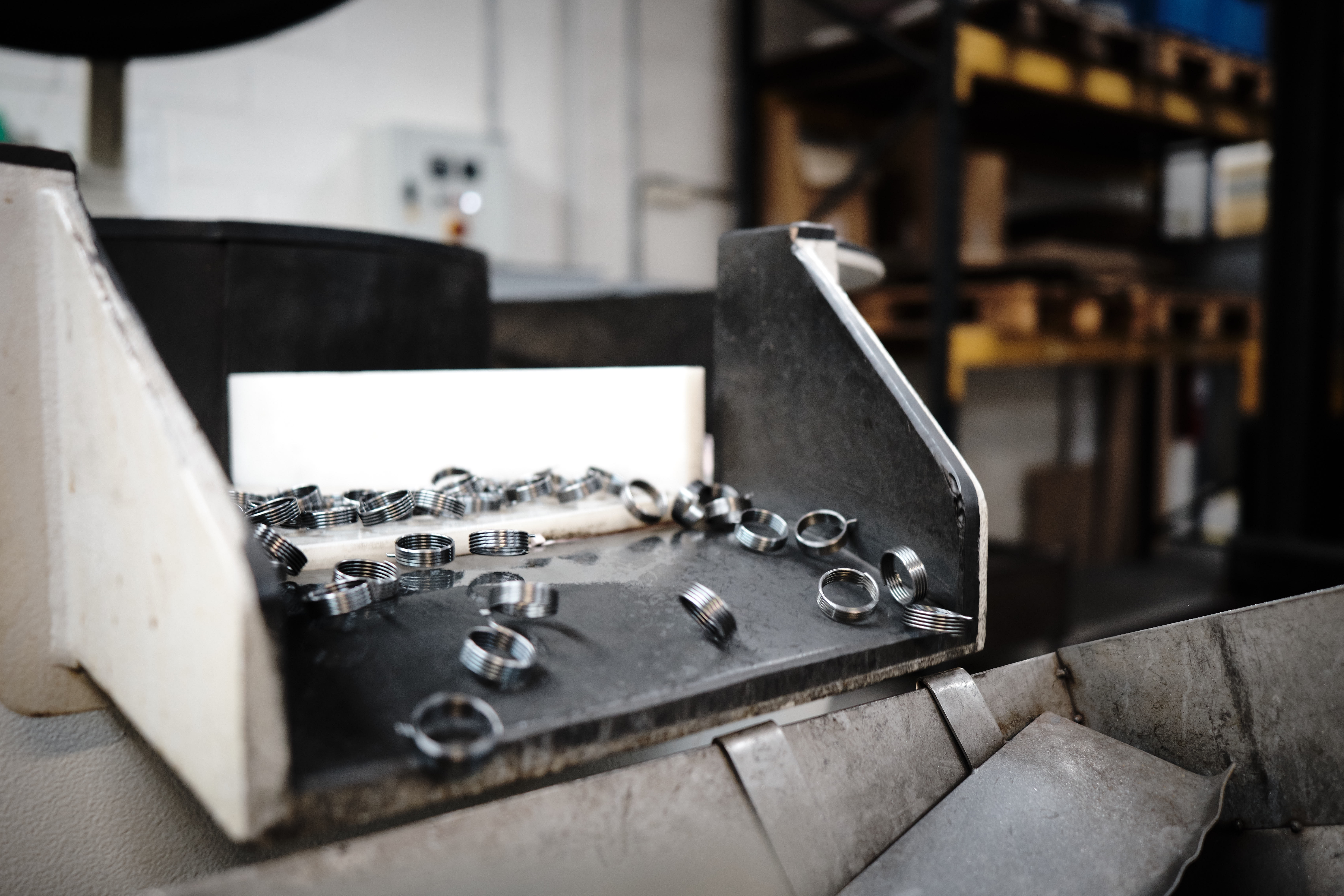 Small metal coil springs move along a conveyor belt and through a chute into a container on a production line.