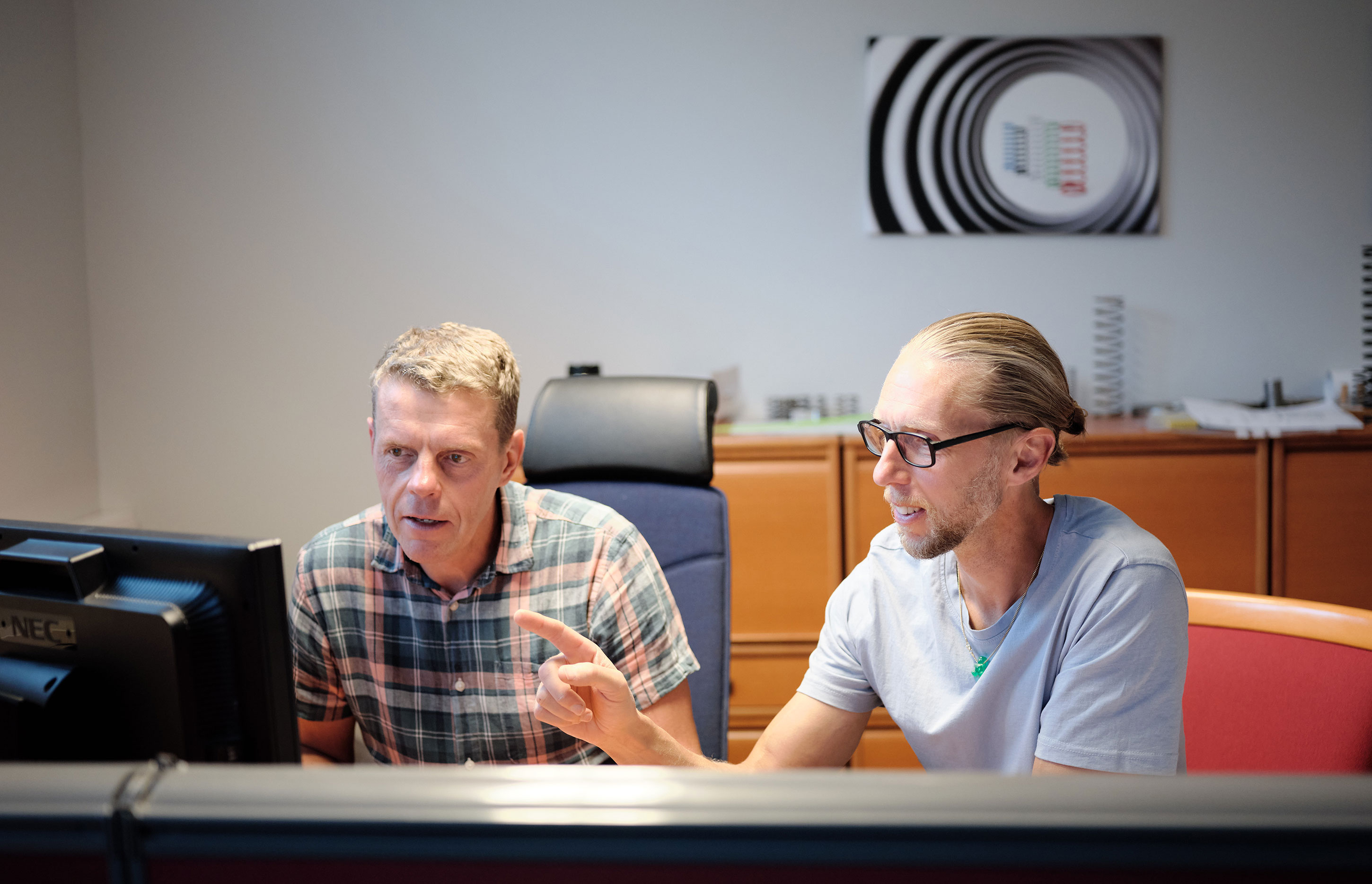 Two colleagues sitting at a desk, discussing content on a computer screen.